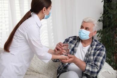 Doctor giving water to senior man with protective mask at nursing home