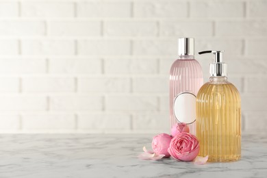 Photo of Stylish dispenser with liquid soap, bottle of shower gel and flowers on white marble table, space for text