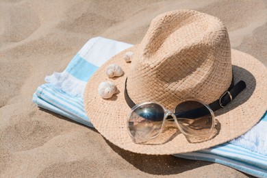 Photo of Straw hat with seashells, sunglasses and beach towel on sand