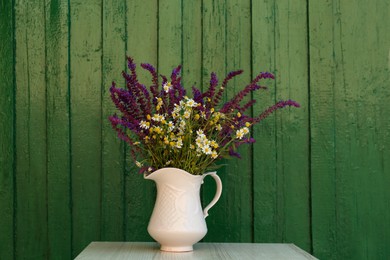 Beautiful bouquet with field flowers in jug on white wooden table