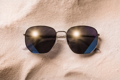 Stylish sunglasses on white sand, top view