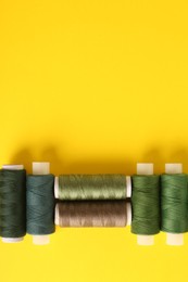 Photo of Different shades of green sewing threads on yellow background, flat lay. Space for text