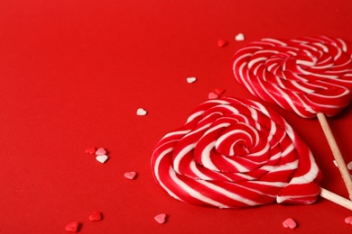 Sweet heart shaped lollipops and sprinkles on red background, closeup view with space for text. Valentine's day celebration