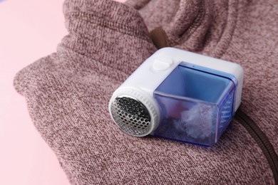 Photo of Fabric shaver and sweater on pink background, closeup