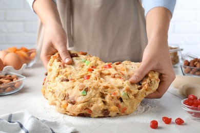 Woman kneading dough with candied fruits and nuts for Stollen at white table, closeup. Baking traditional German Christmas bread