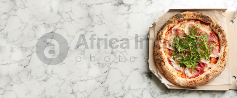 Tasty pizza with meat and arugula in cardboard box on white marble table, top view with space for text. Banner design
