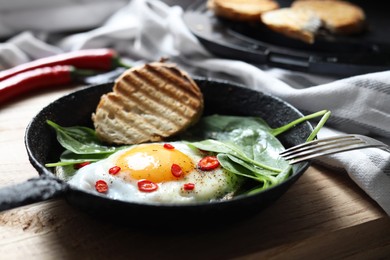 Photo of Delicious fried egg with spinach and chilli served on wooden table, closeup