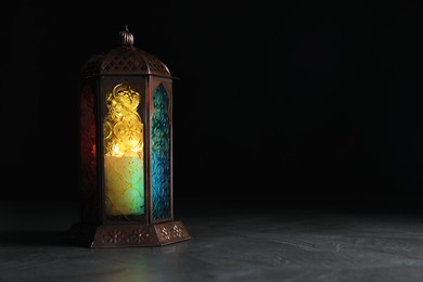 Decorative Arabic lantern on grey table against black background, space for text