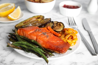 Photo of Tasty cooked salmon and vegetables served on white marble table. Healthy meals from air fryer