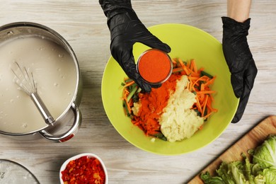Photo of Woman preparing spicy cabbage kimchi at wooden table, top view