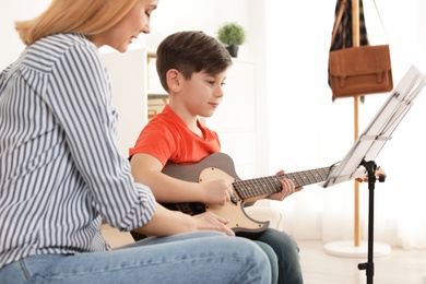 Little boy playing guitar with his teacher at music lesson. Learning notes