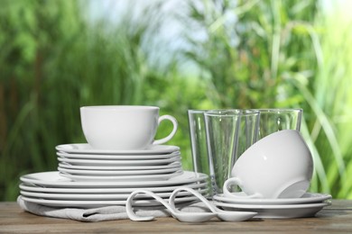 Photo of Set of clean dishware and glasses on wooden table against blurred background, space for text