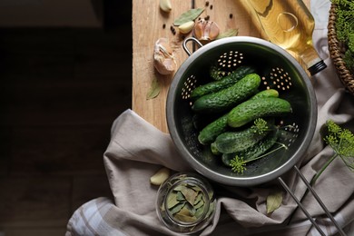 Photo of Fresh cucumbers in colander and other ingredients prepared for canning on wooden table, flat lay. Space for text