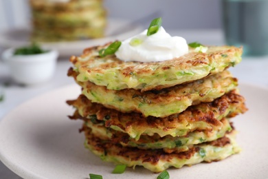 Delicious zucchini fritters with sour cream in plate, closeup view
