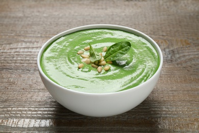 Bowl of healthy green soup with fresh spinach on wooden table