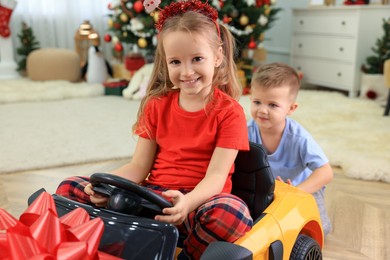 Cute little boy pushing toy car with his sister in room decorated for Christmas