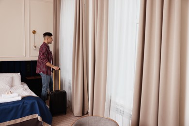 Handsome man with suitcase near window in hotel room