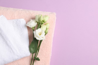 Soft folded towels with flowers on violet background, top view. Space for text