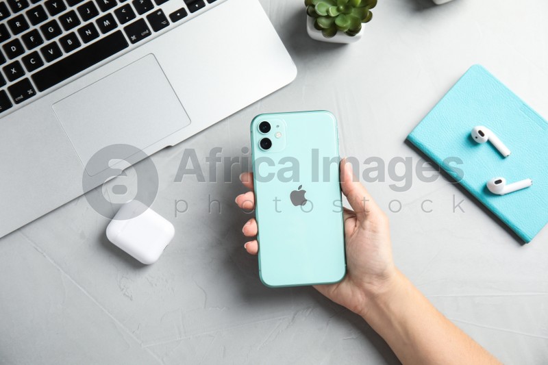 Photo of MYKOLAIV, UKRAINE - JULY 10, 2020: Woman holding Iphone 11 Green at table, top view