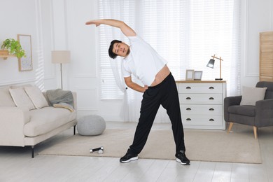Overweight man stretching near sofa in living room