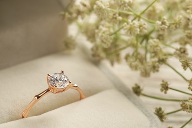Photo of Beautiful engagement ring with gemstone in box and flowers on table, closeup