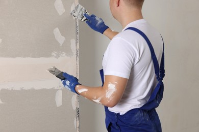 Man plastering wall with putty knife indoors, closeup. Home renovation