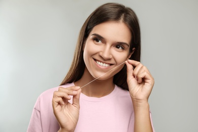 Young woman flossing her teeth on light grey background. Cosmetic dentistry
