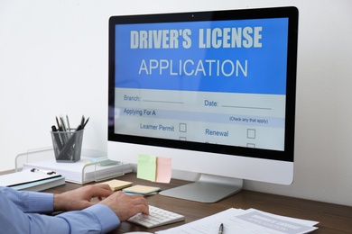 Man using computer to fill driver's license application form at table in office, closeup