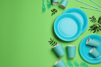 Photo of Flat lay composition with disposable tableware on green background, space for text