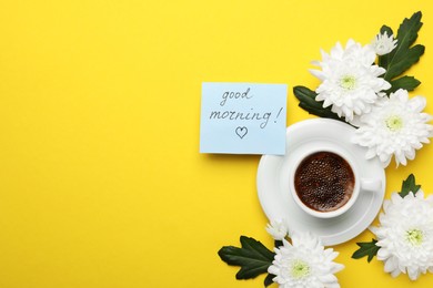 Cup of aromatic coffee, beautiful white chrysanthemums and Good Morning note on yellow background, flat lay. Space for text