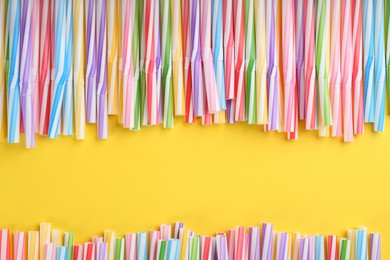 Heap of colorful plastic drinking straws on yellow background, flat lay. Space for text
