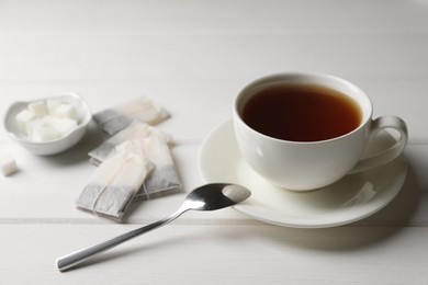 Tea bags and sugar near cup of hot drink on white wooden table