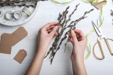 Woman making beautiful bouquet of pussy willow branches at white wooden table, top view