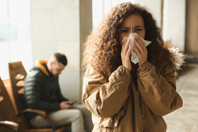 Young African-American woman sneezing indoors. Influenza virus