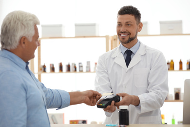Customer using terminal for contactless payment with credit card in pharmacy