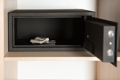 Open steel safe with money and smartphone in wooden closet