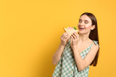 Photo of Young woman eating tasty sandwich on yellow background. Space for text