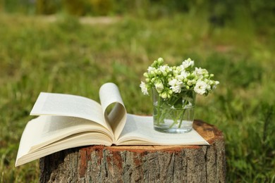 Photo of Open book and glass with flowers on tree stump outdoors