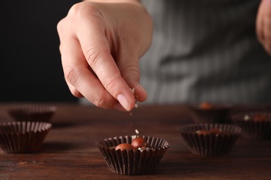 Photo of Professional confectioner making delicious chocolate candies with hazelnuts at wooden table, closeup
