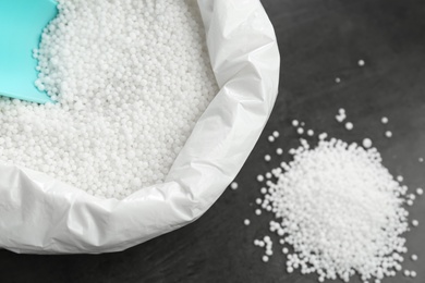 Bag with granular mineral fertilizer and scoop on grey background, closeup