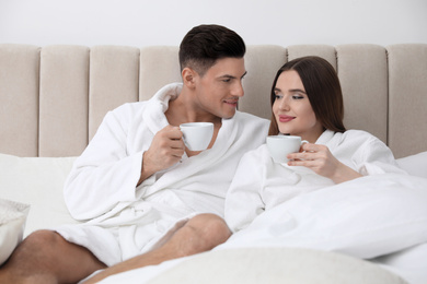 Happy couple in bathrobes with coffee on bed at home