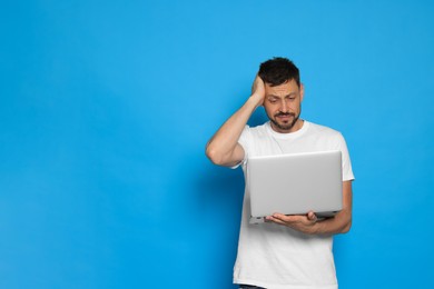 Confused man looking at laptop on light blue background. Space for text