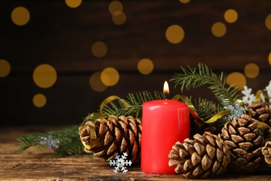 Burning candle, pine cones and fir tree branches on wooden table against blurred festive lights, space for text. Christmas eve