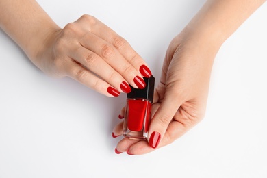 Woman with bright manicure holding bottle of nail polish on white background, closeup