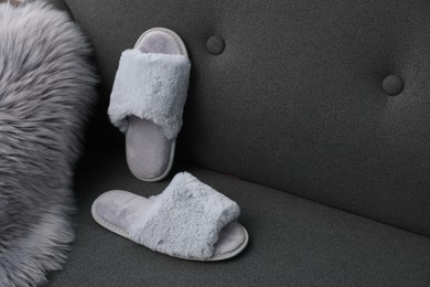 Photo of Soft grey slippers and faux fur on sofa, space for text