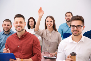 Young woman raising hand to ask question at business training on white background
