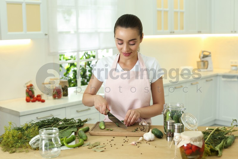 Photo of Woman cutting cucumber at table in kitchen. Preparing pickles