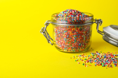 Colorful sprinkles in jar on yellow background, space for text. Confectionery decor
