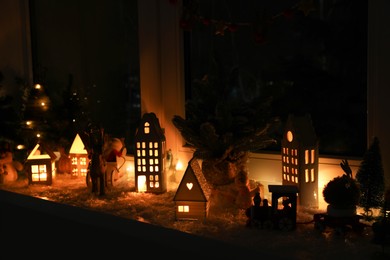 Photo of Christmas atmosphere. Beautiful glowing houses and toys on window sill indoors