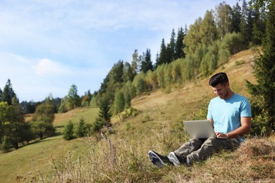 Man working with laptop outdoors surrounded by beautiful nature. Space for text